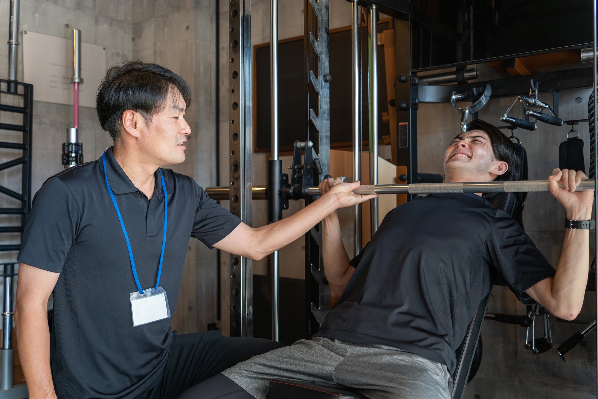 トレーナーがマンツーマンでベンチプレスの補助をしている様子