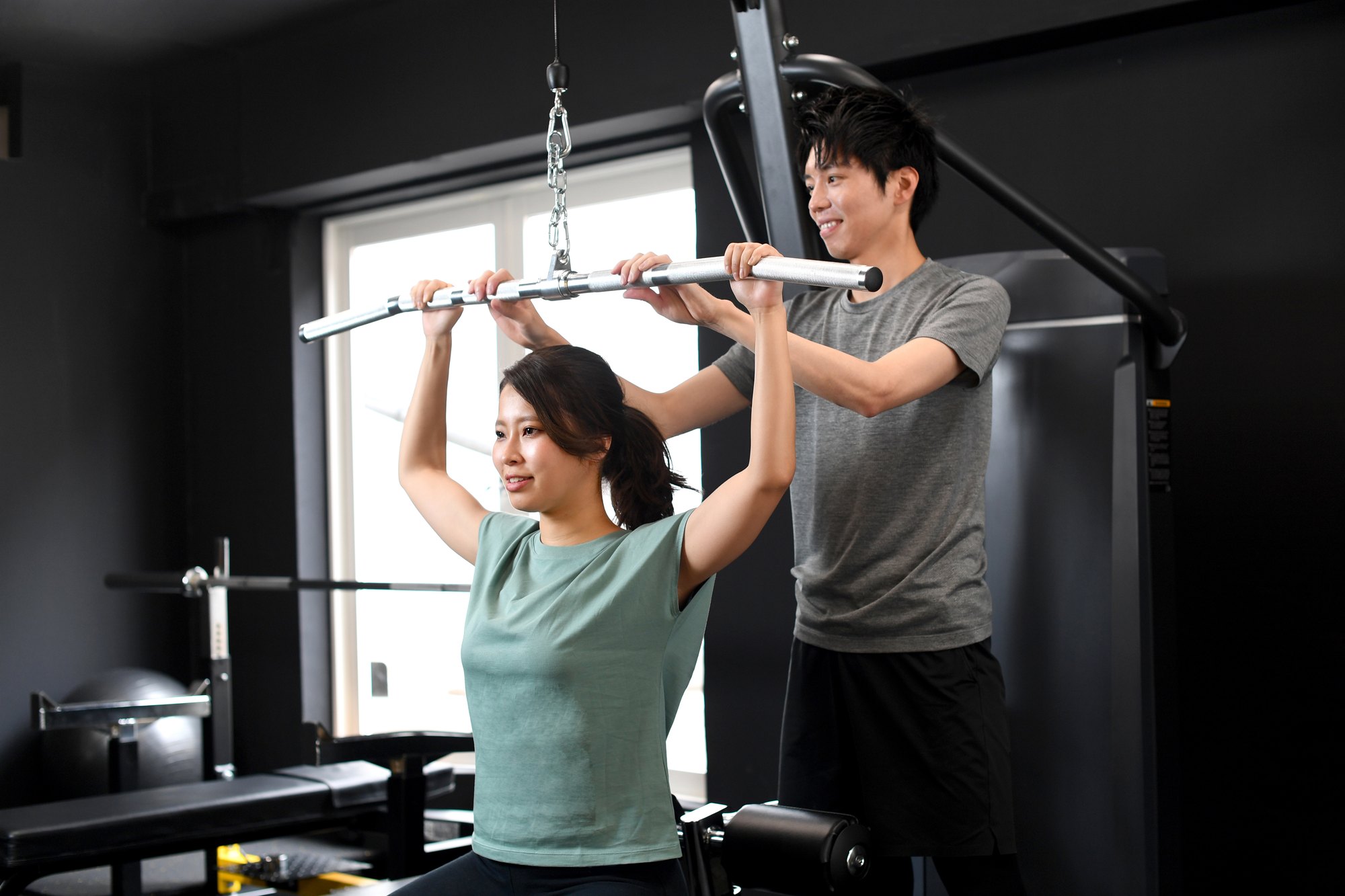 トレーナーがフォームを確認しながらマシントレーニングを指導している様子